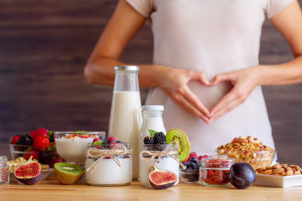 Beeren, Früchte, Nüsse und Milchprodukte für das Mikrobiom auf einem Tisch, dahinter eine Person, die mit ihren Händen ein Herz vor ihrem Magen formt