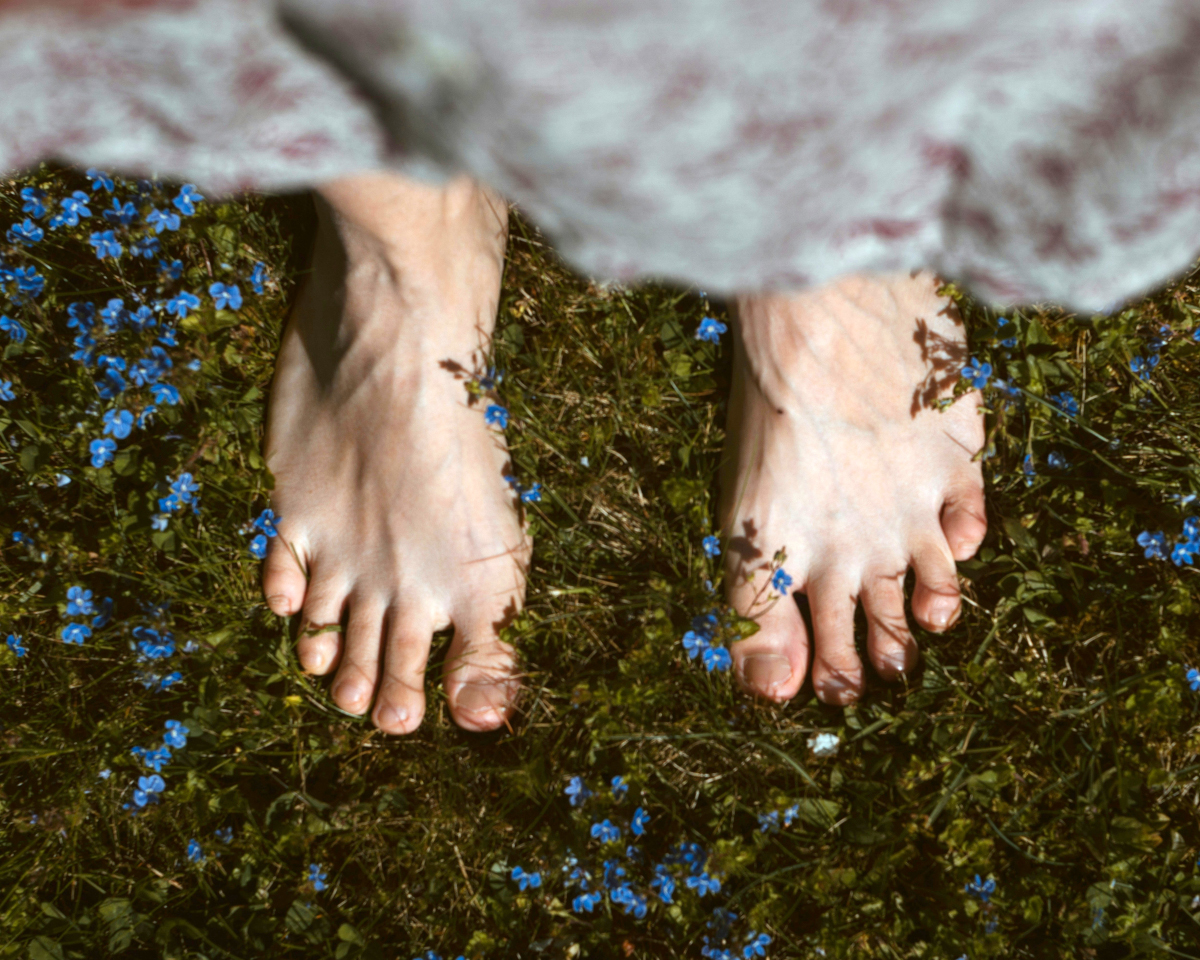 Nackte Füße auf feuchter Wiese, umgeben von Blumen mit kleinen blauen Blüten