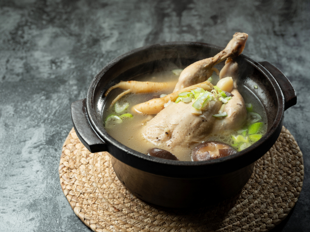 Asiatische klare Suppe mit Geflügel, Pilzen, Kräutern und Ginsengwurzel auf runder Korkmatte