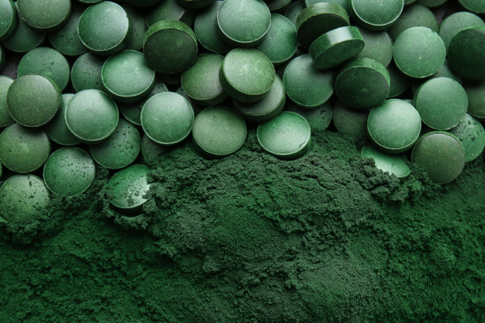 Spirulina-Tabletten in der oberen Bildhälfte liegen auf Spirulina-Pulver