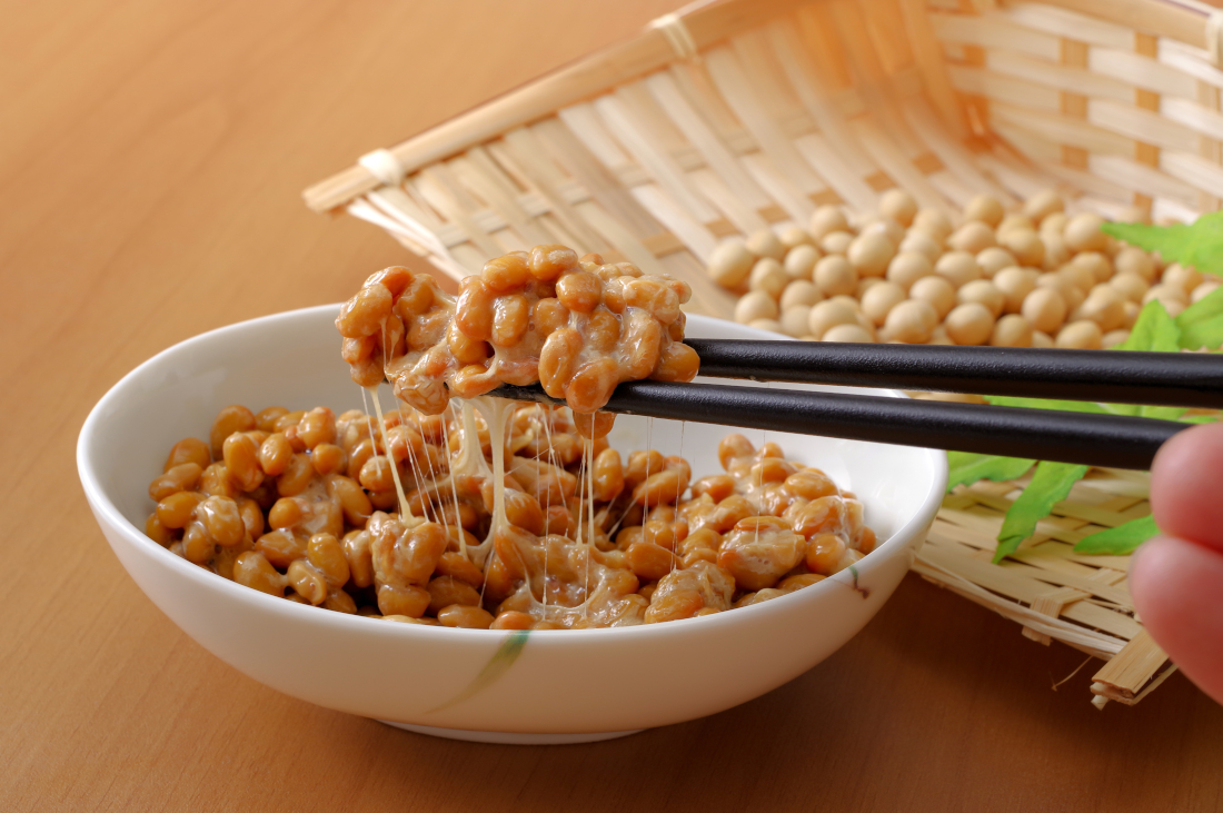 Weiße Schüssel mit Natto, das zwischen der Portion auf den Esstäbchen und der Portion in der Schüssel Fäden zieht.