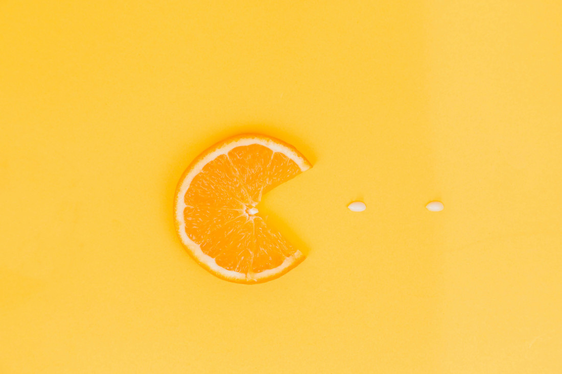 Eine Scheibe von einer Orange, aus der ein Dreieck geschnitten wurde, auf gelber Oberfläche