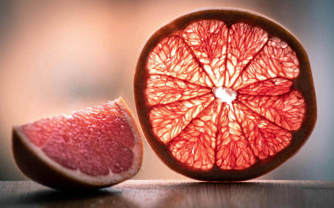 Foto von stehender Grapefruitscheibe, von hinten beleuchtet, daneben Grapefruitspalt