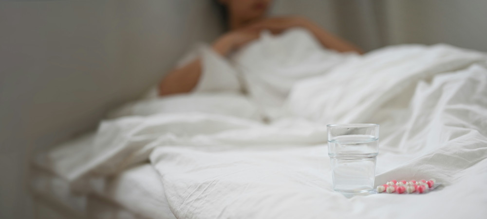 Person im Bett, davor Wasserglas mit Kapseln daneben